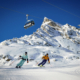 Zwei Personen Fahren auf der Skipiste und im Hintergrund sieht man die Berge.